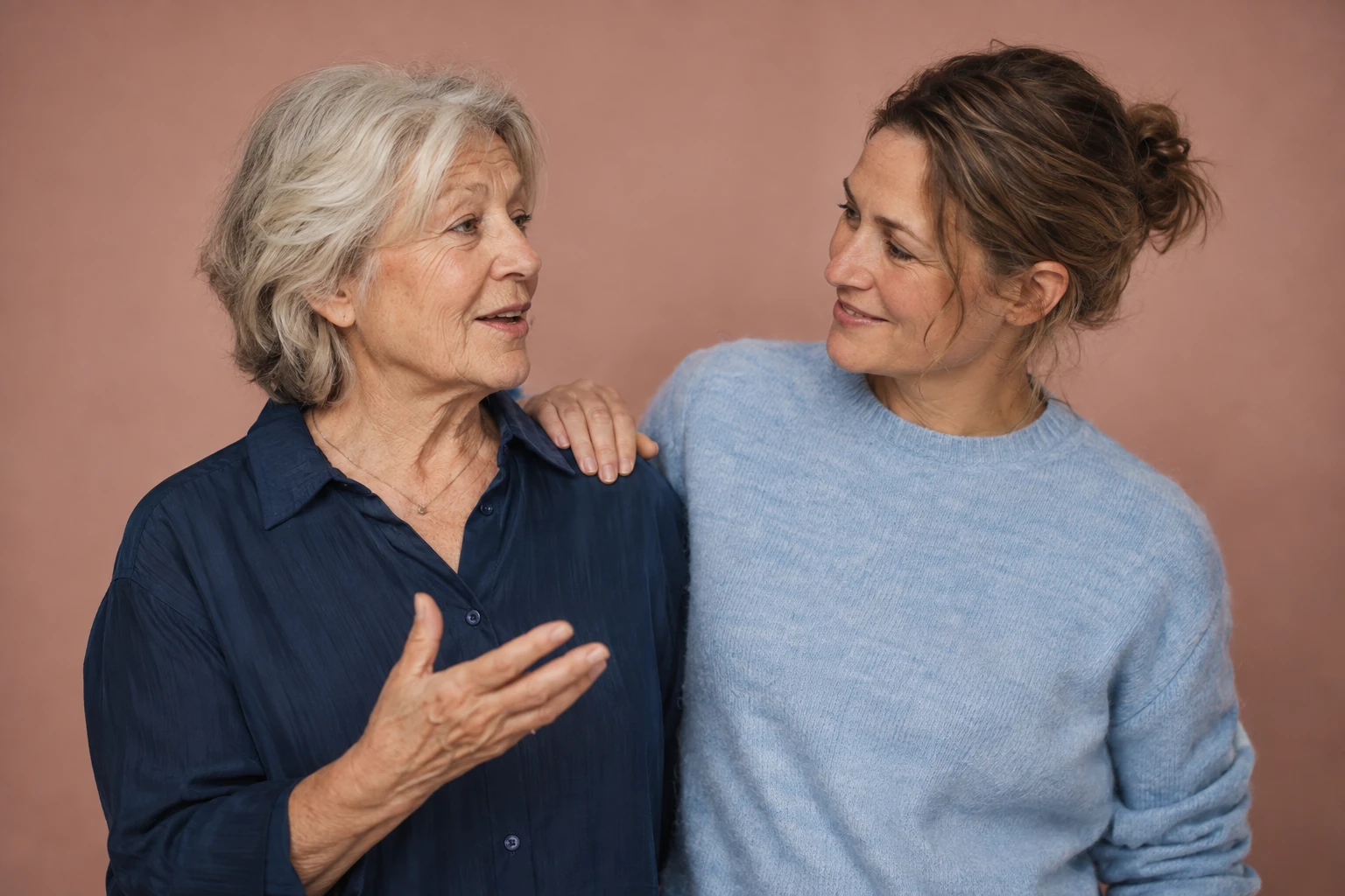 Older woman talking with a younger woman whose hand rests on her shoulder.